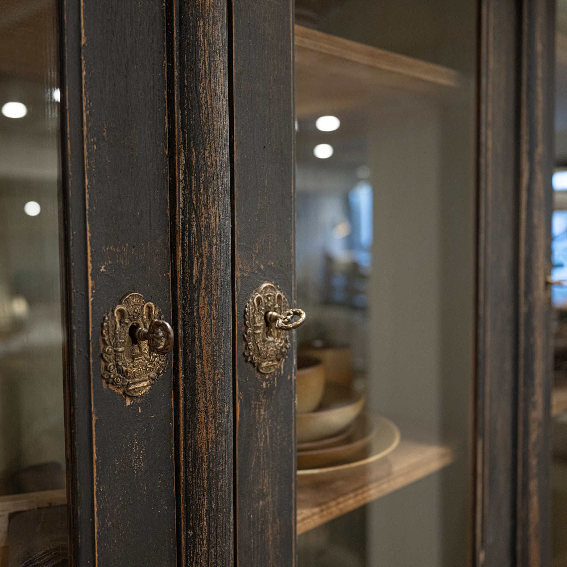Antique-style brass door handles with ornate designs on dark-stained wooden cabinet doors of late 19th century french display cabinet