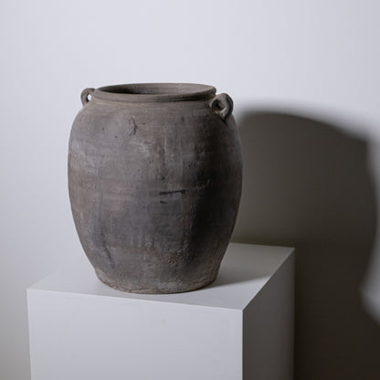 The 19th Century Central European Clay Pot, with its large round shape and two small handles by the rim, sits atop a white pedestal, adding antique charm to any decor with its dark clay finish and historic appeal.