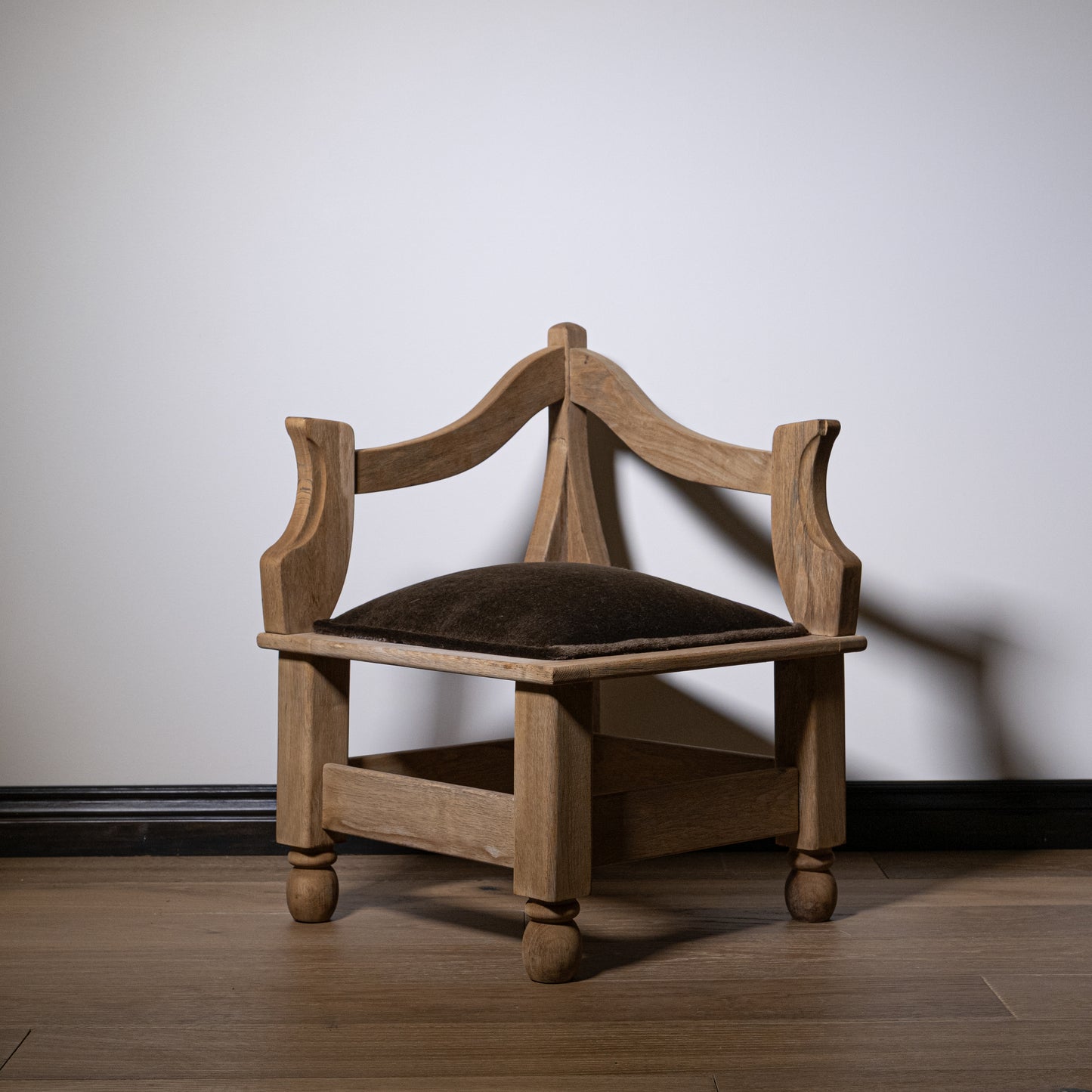 A rustic carved wood corner stool with a dark mohair seat and turned legs for comfortable seating