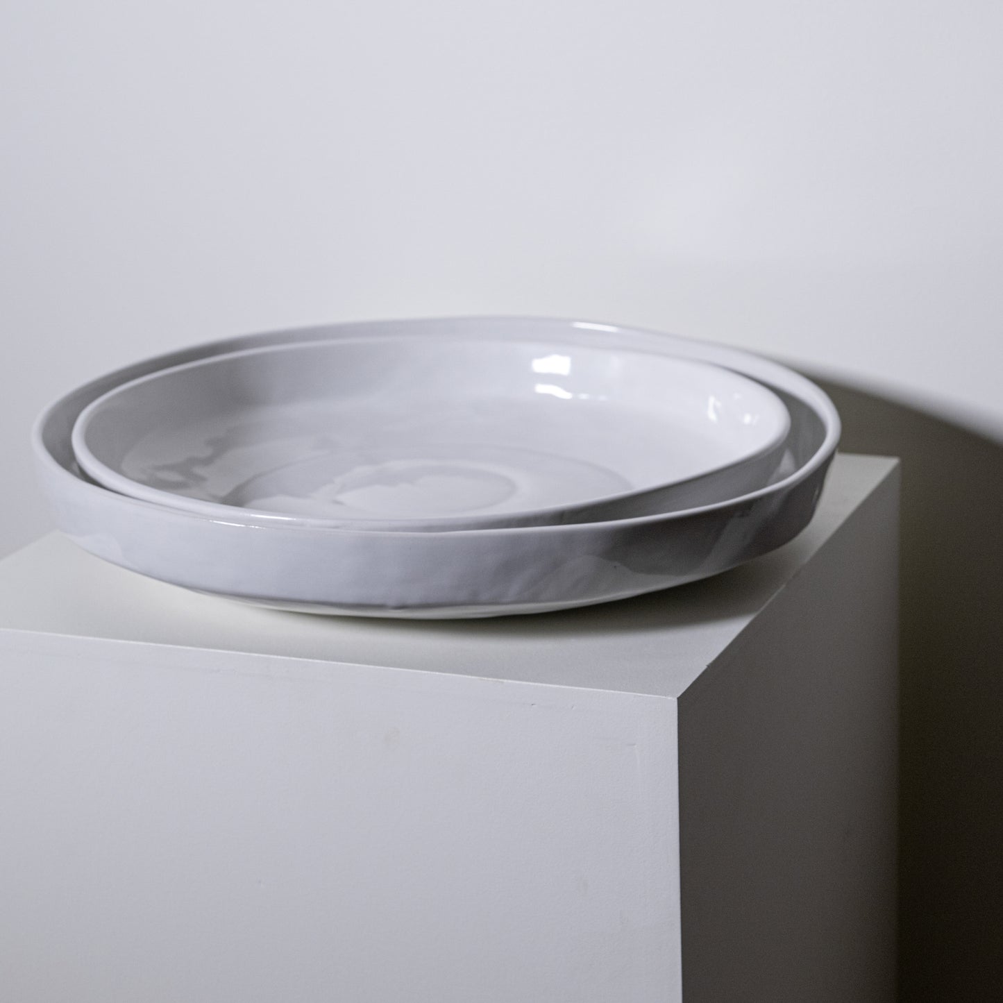 Two nested white ceramic bowls with subtle gray marbled rims displayed on a minimalist pedestal in cottonwood platter no 316