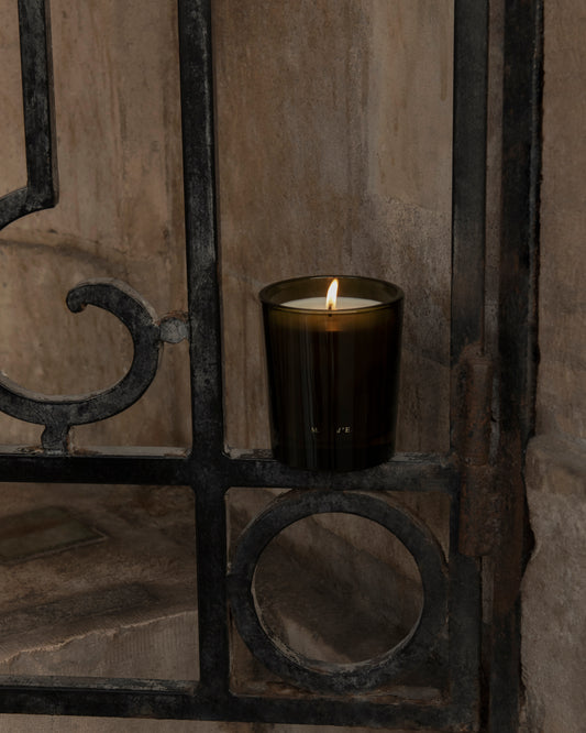 A lit amber glass candle with sleek minimalist design from maison detto candle rotano collection