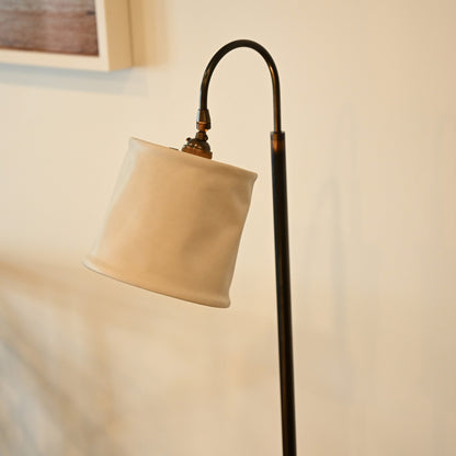 Cream-colored fabric lampshade with curved black metal stand on brass and leather floor lamp