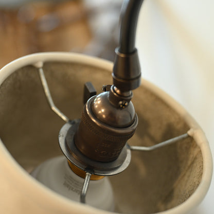 Antique brass lamp socket with black cord and metal bracket inside cream fabric shade of brass and leather floor lamp