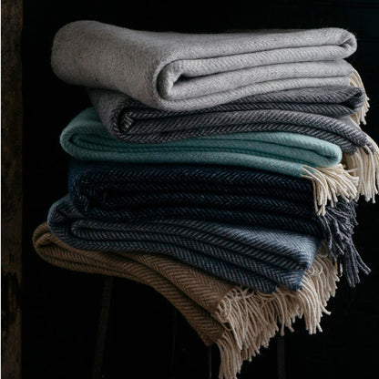 Stack of folded wool herringbone throw blankets in muted harvest tones with cream-colored fringe