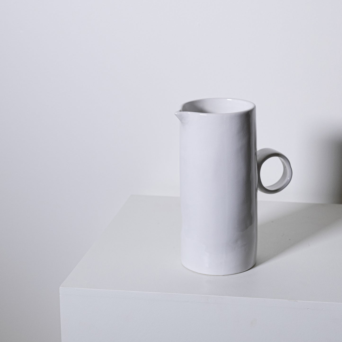 A sleek minimalist white ceramic fir pitcher no 923 with a smooth cylindrical body and simple circular handle