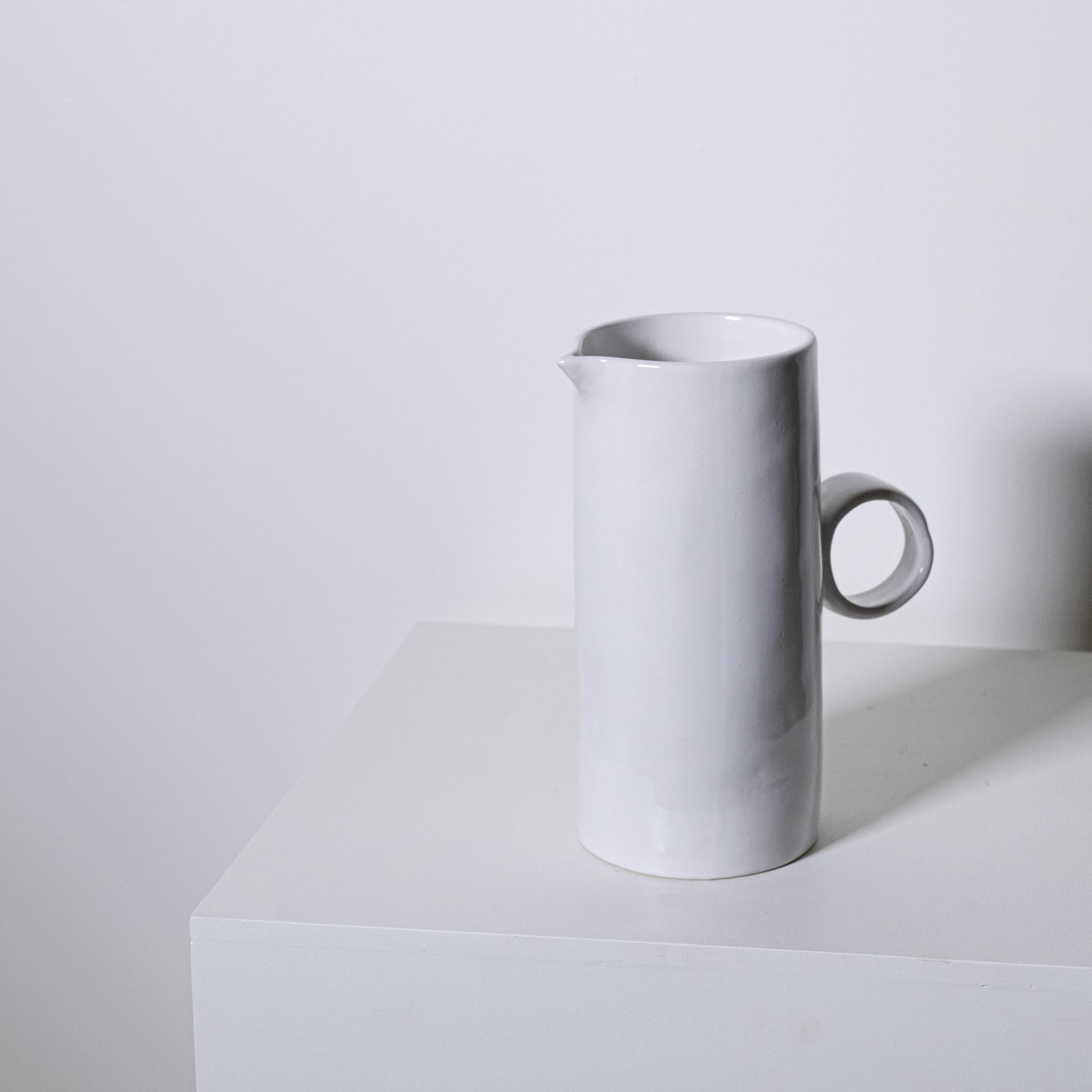 A sleek minimalist white ceramic fir pitcher no 923 with a smooth cylindrical body and simple circular handle
