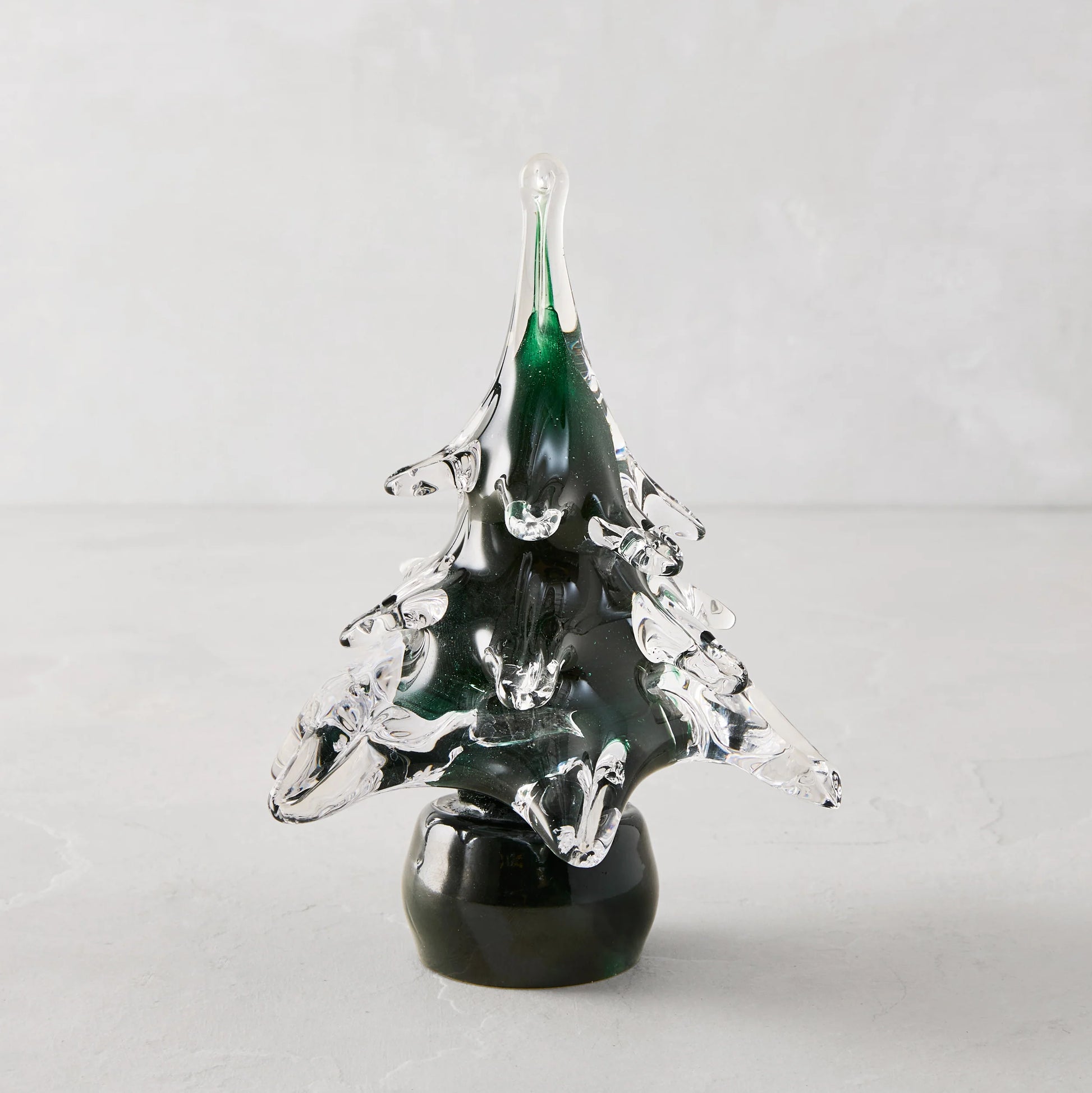 Green glass pine tree ornament made of translucent green and clear glass with a glossy black base for christmas decor