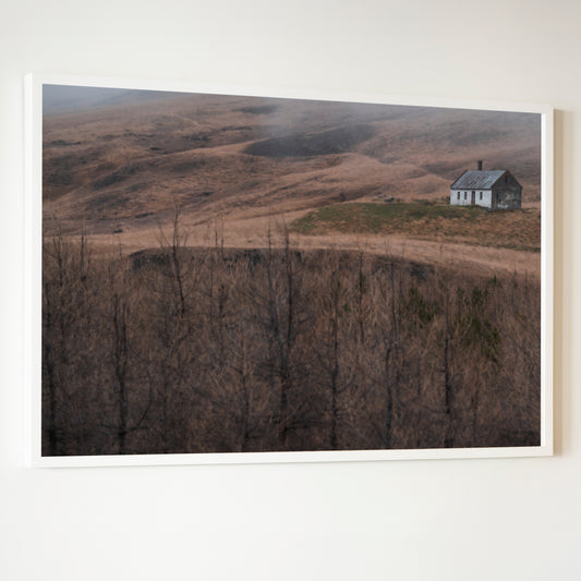 White-framed photograph titled House of Silence showing a solitary weathered house with dark roof in a barren landscape