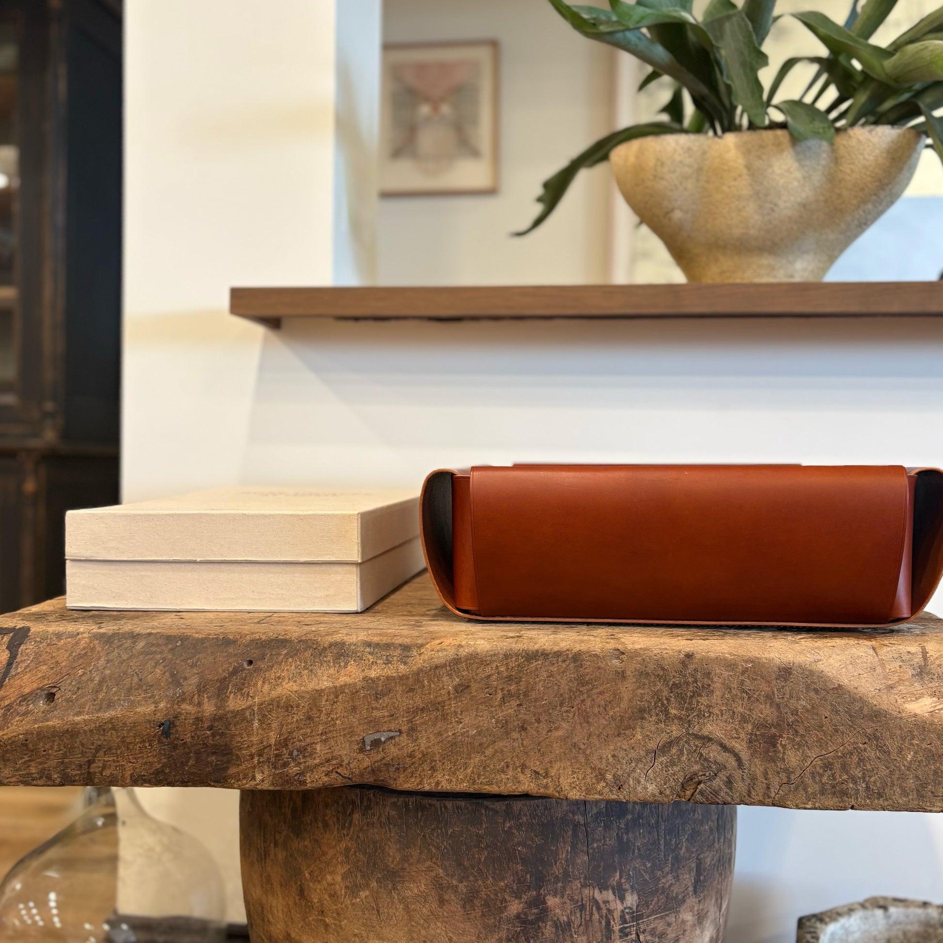 A sleek rust-colored leather assembly basket with a minimalist design resting on a rustic wooden surface