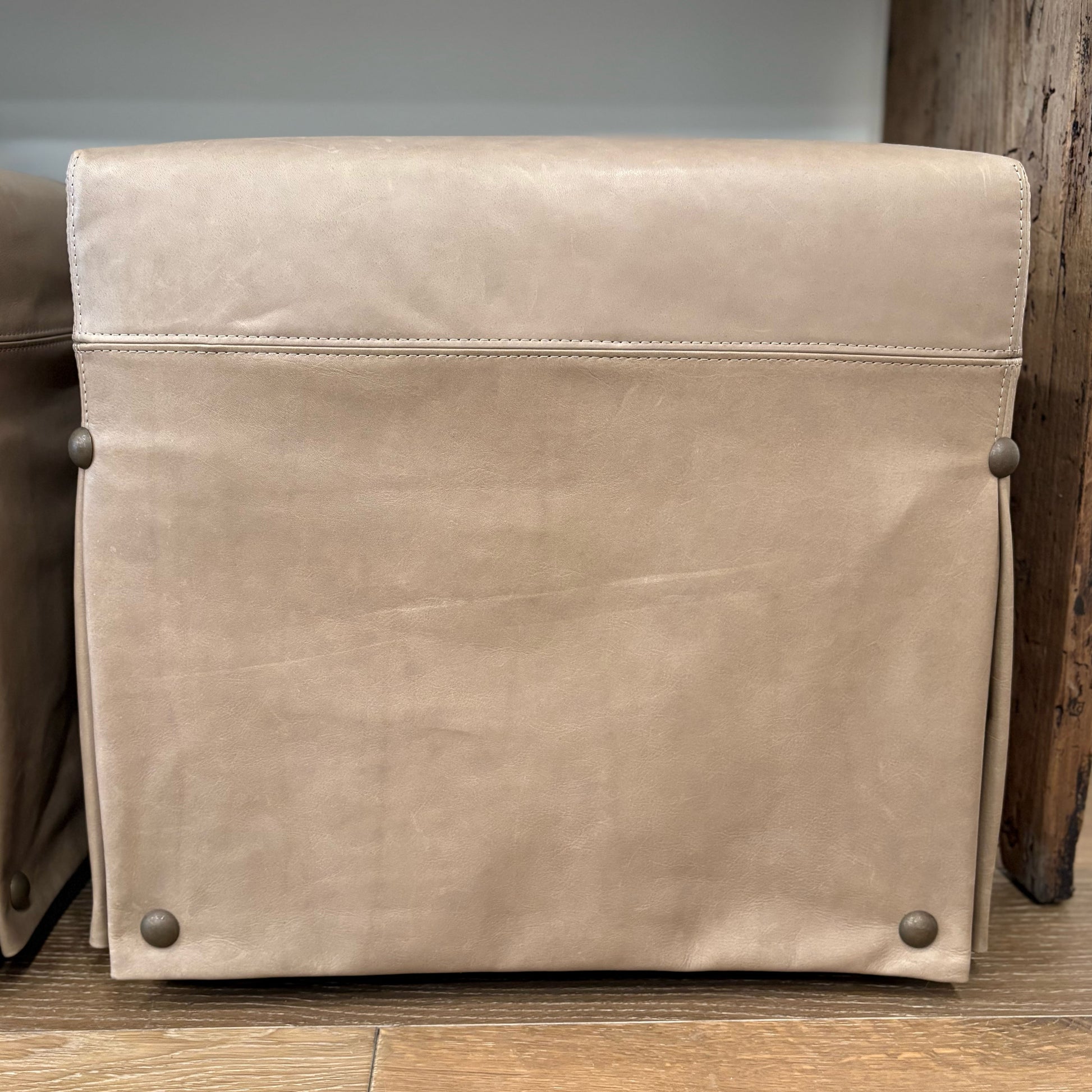 Beige leather satchel with subtle stitching and metallic rivets at corners paired with kim leather slipcovered ottoman with nailhead detail floor model