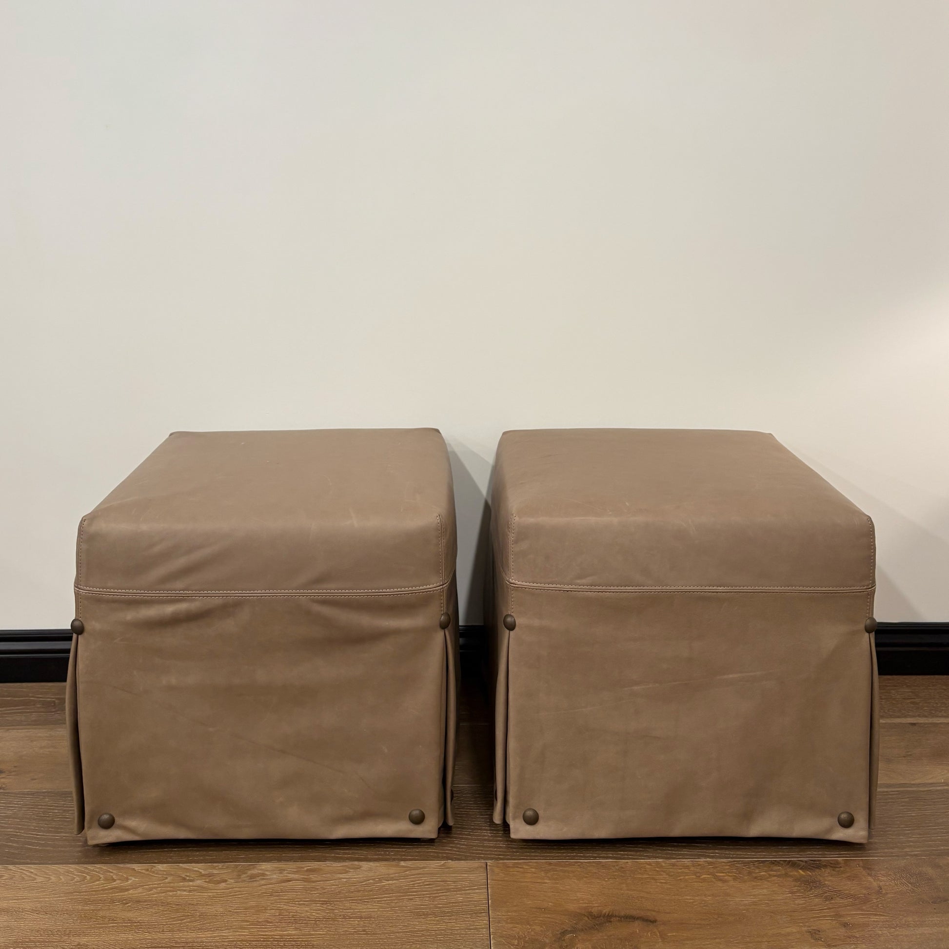 Two taupe leather kim slipcovered ottomans with pleated skirts and brass nailhead detail floor model