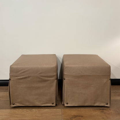 Two taupe leather kim slipcovered ottomans with pleated skirts and brass nailhead detail floor model