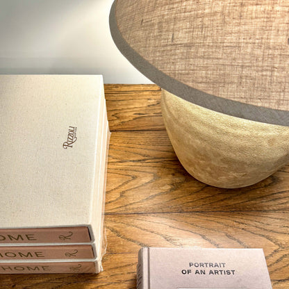 Beige linen-covered book with rizzoli embossed in gold lettering shown with mid century shanxi clay pot table lamp