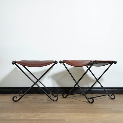 Two brown stools with black metal frames on a wooden floor against a white wall.