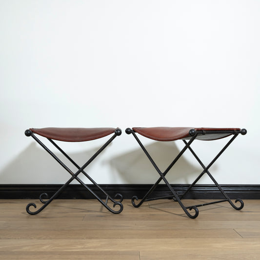 Two brown stools with black metal frames on a wooden floor against a white wall.