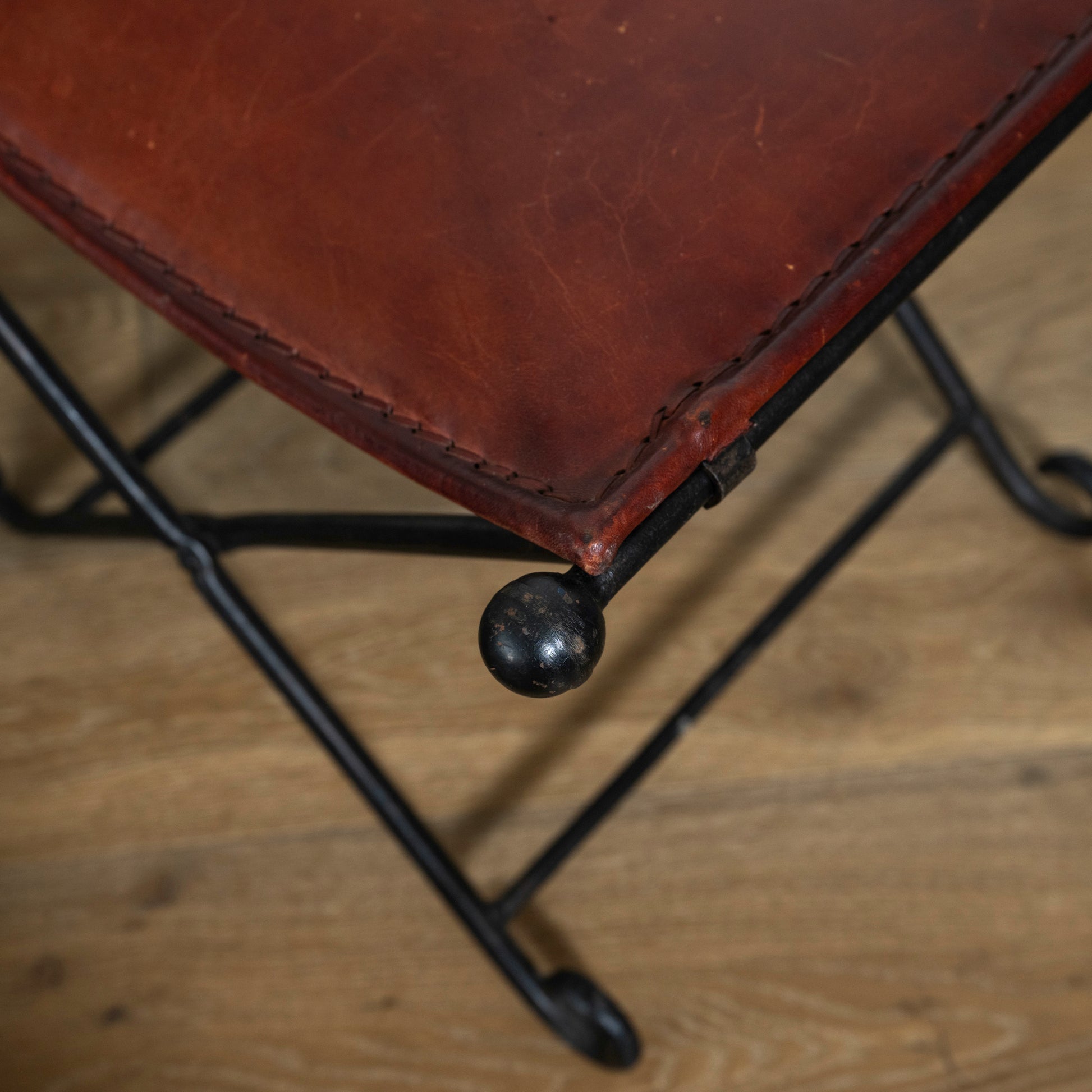 Close-up of a brown leather stool with metal legs on a wooden floor.