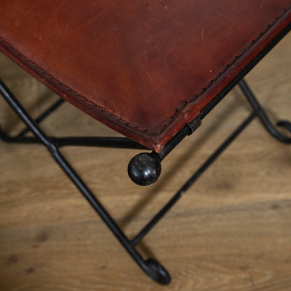 Close-up of a brown leather stool with metal legs on a wooden floor.