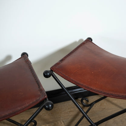 Two brown leather stools with black metal legs on a plain background