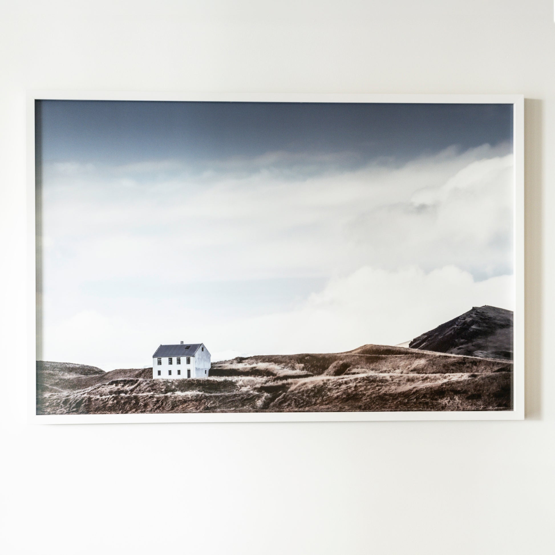 Framed photograph of a house on a hillside with clouds in the sky