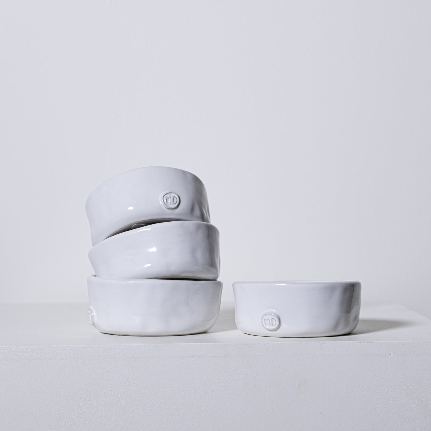 Stack of four matte white ceramic linden bowls with textured rims and small circular logos on each bowl