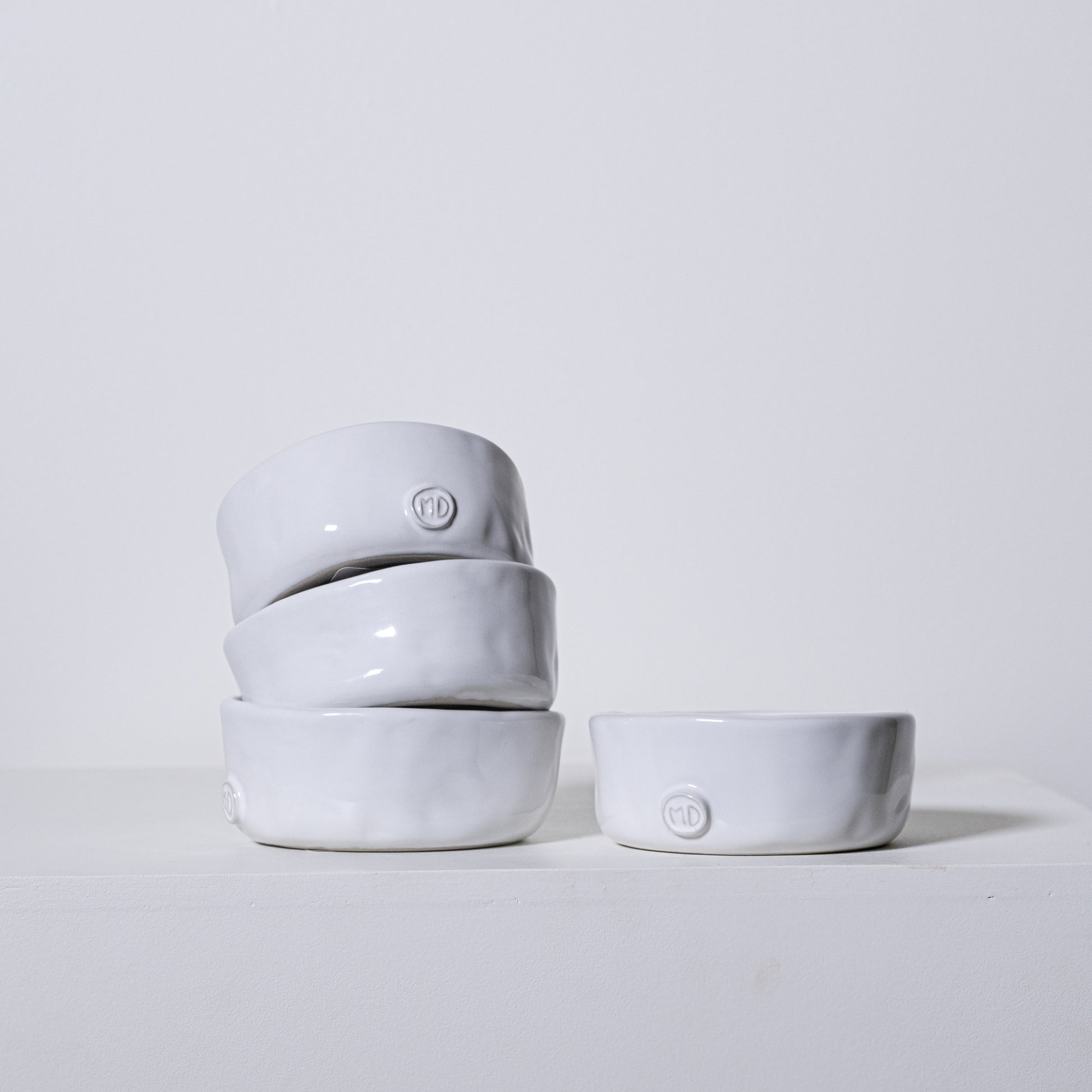 Stack of four matte white ceramic linden bowls with textured rims and small circular logos on each bowl
