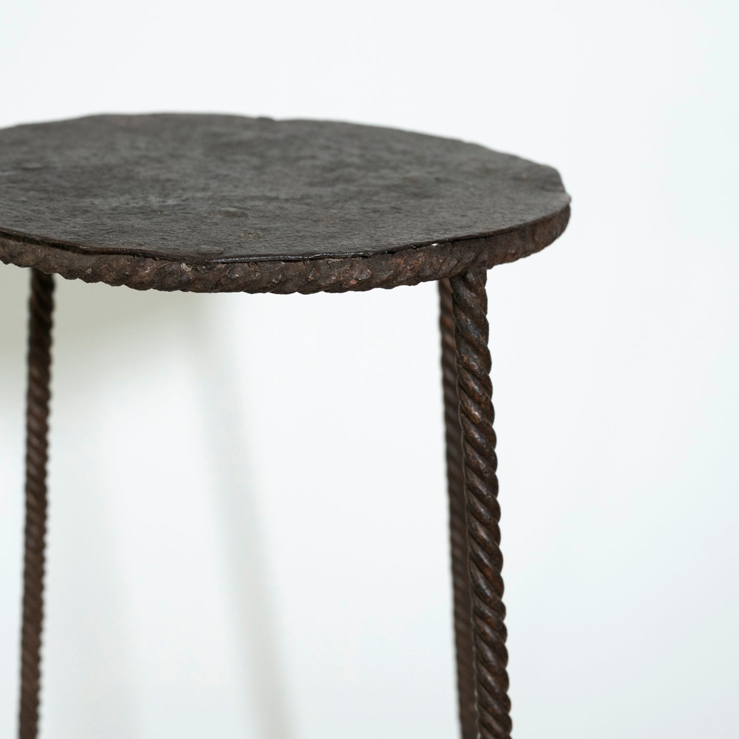 Round side table with textured surface and rope-like legs on a white background