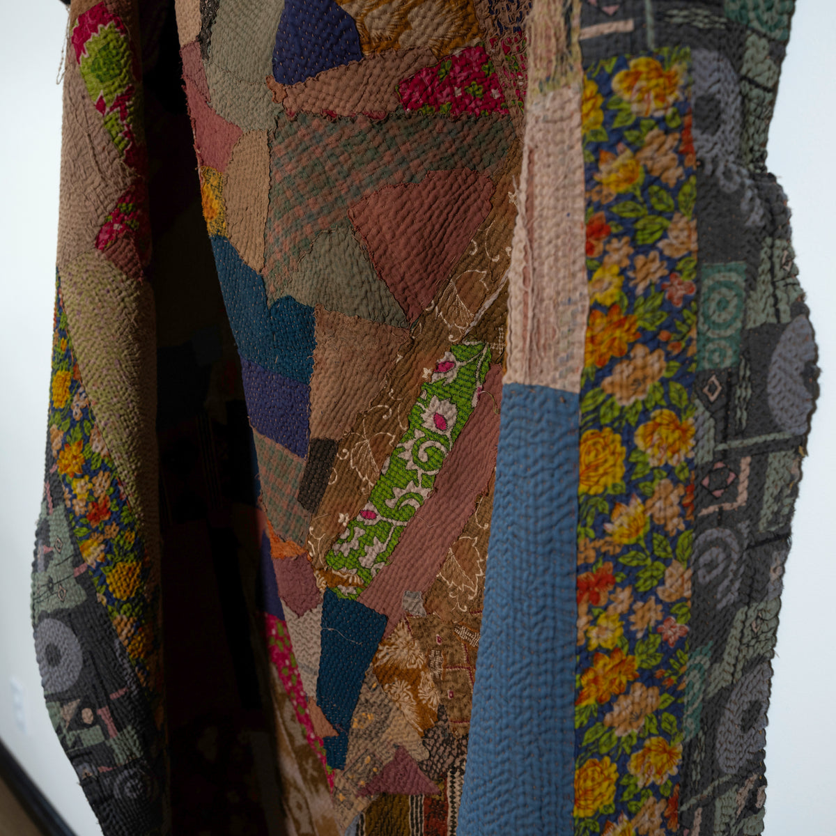A close-up of a patchwork quilt or textile with mixed floral and geometric patterns in earthy tones.