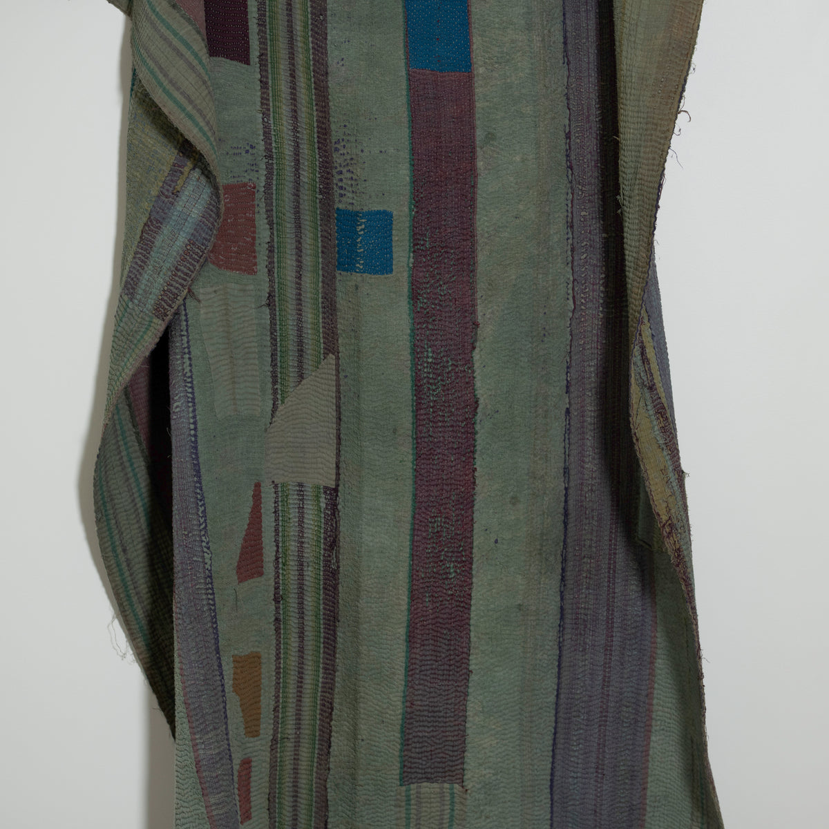 A close-up of a quilt in muted olive green, gray, burgundy, blue, and beige tones