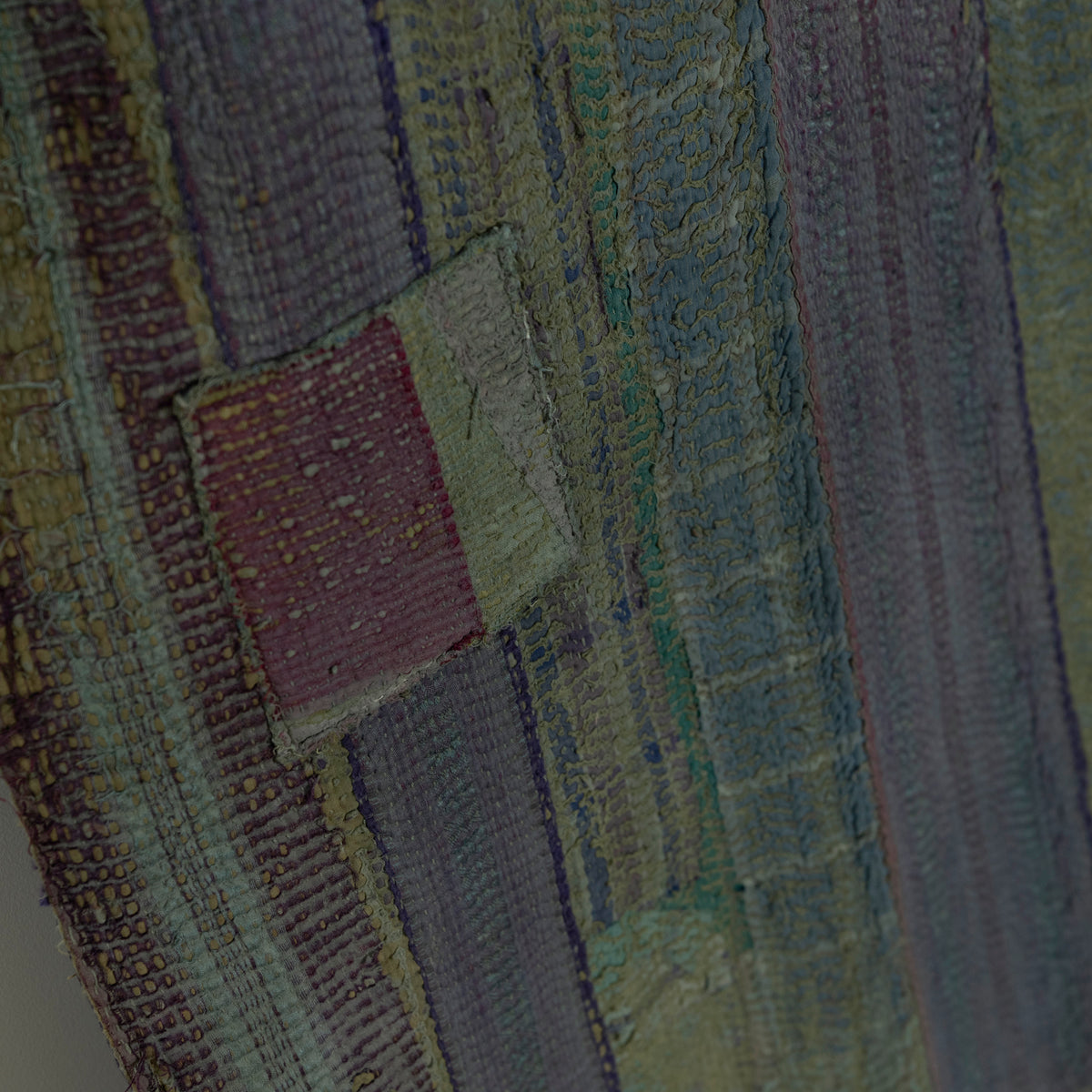 Close-up of a textured quilt with vertical striped panels in muted olive green.