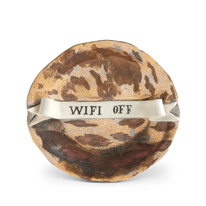 A round crackled ceramic ruan hoffman wifi off plate with brown gold glaze and a white ribbon band across center