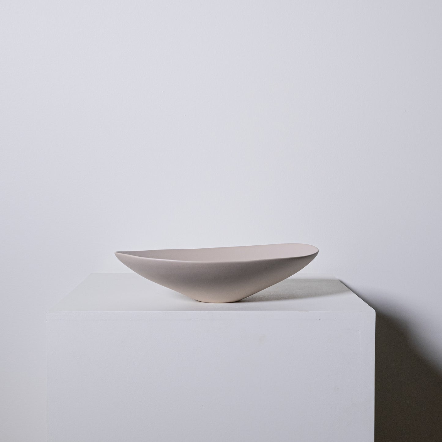 A sleek matte-finished ceramic bowl with modern asymmetrical design in greige color called Baccello Small