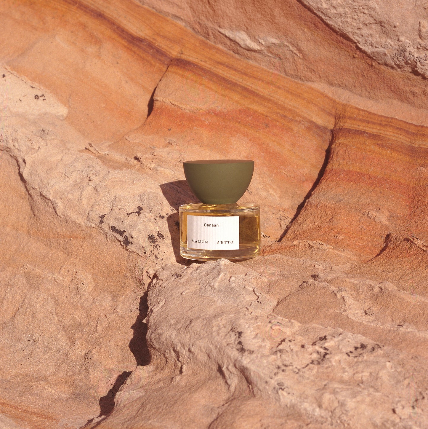 A minimalist glass perfume bottle with matte olive-green cap and white label for Maison dEtto fragrance Canaan