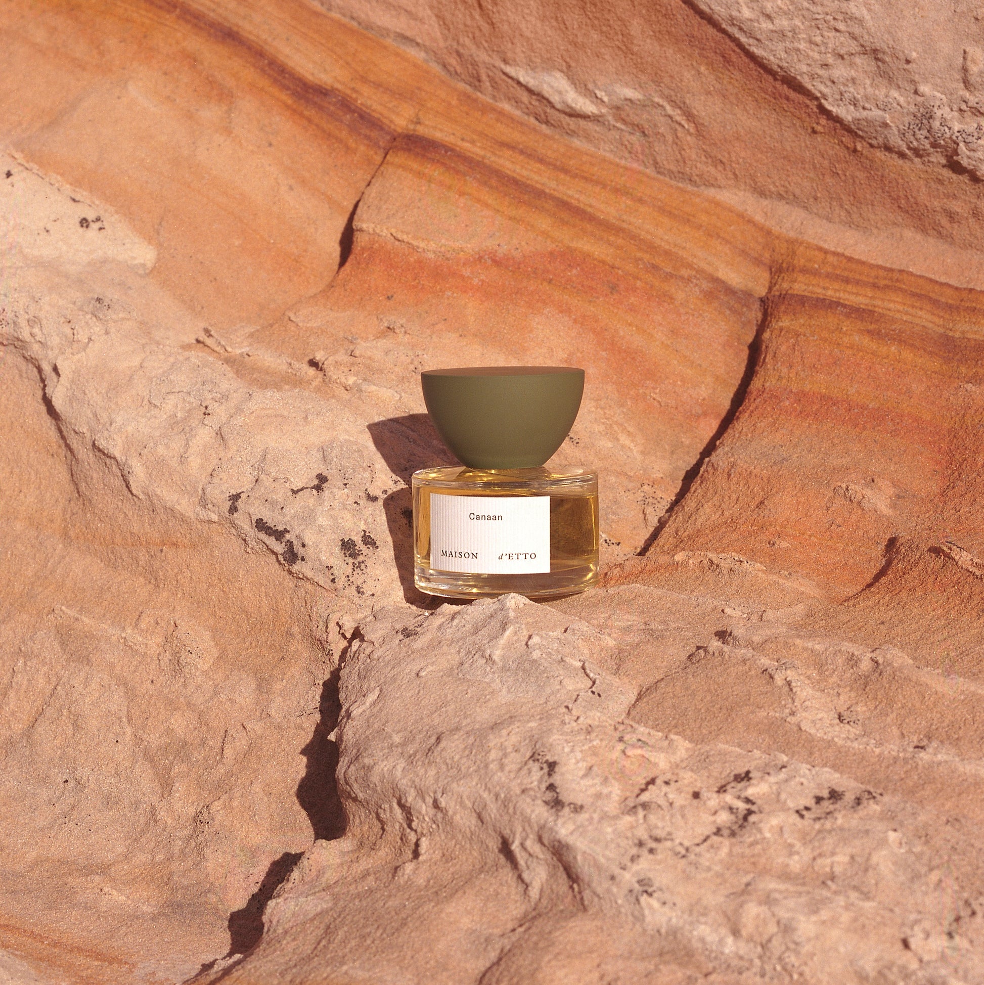 A minimalist glass perfume bottle with matte olive-green cap and white label for Maison dEtto fragrance Canaan