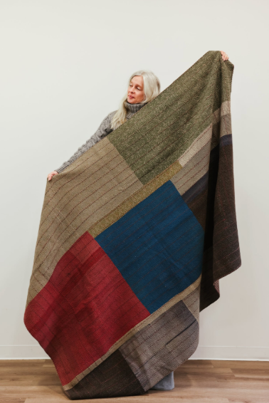 A woman holds a riley quilt patchwork blanket with bold geometric blocks in earthy tones and vibrant accents