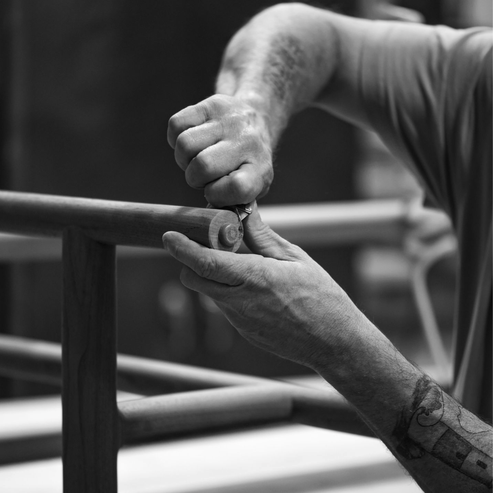A hand holding a chisel, carefully shaping the end of a wooden dowel.