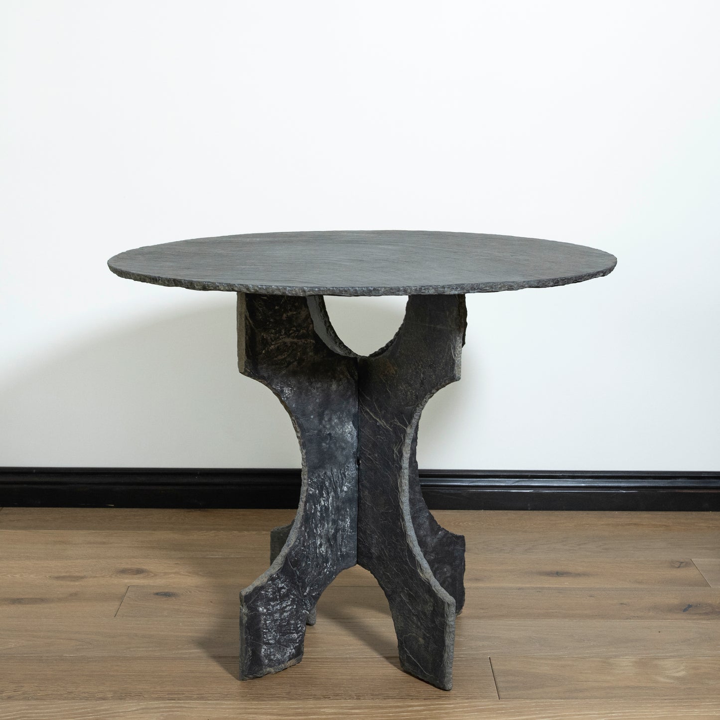 Round stone table with a unique base design on a wooden floor.