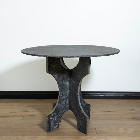 Round stone table with a unique base design on a wooden floor.