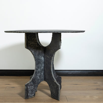 Black marble dining table with unique base design on a wooden floor.