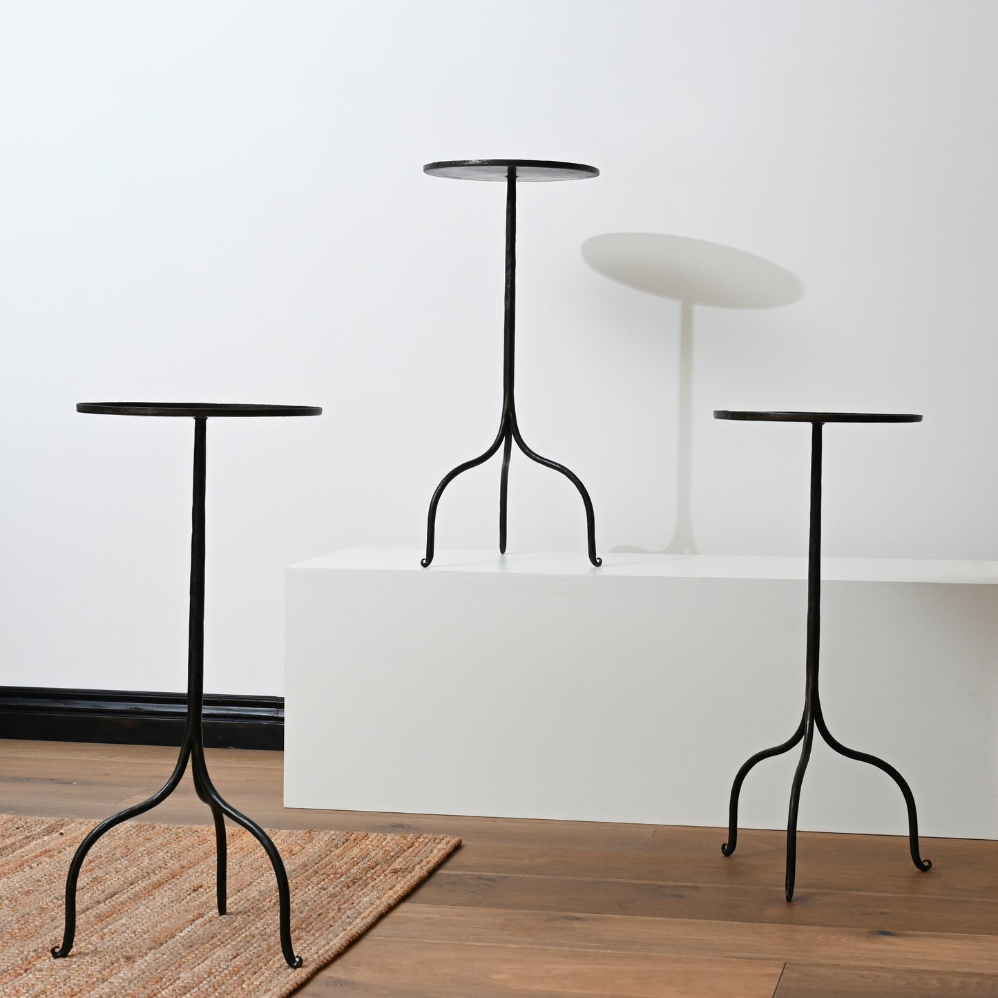 Three black hand forged iron side tables with curved legs and round tops made of wrought iron pedestal style