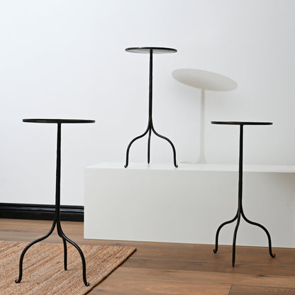 Three black hand forged iron side tables with curved legs and round tops made of wrought iron pedestal style