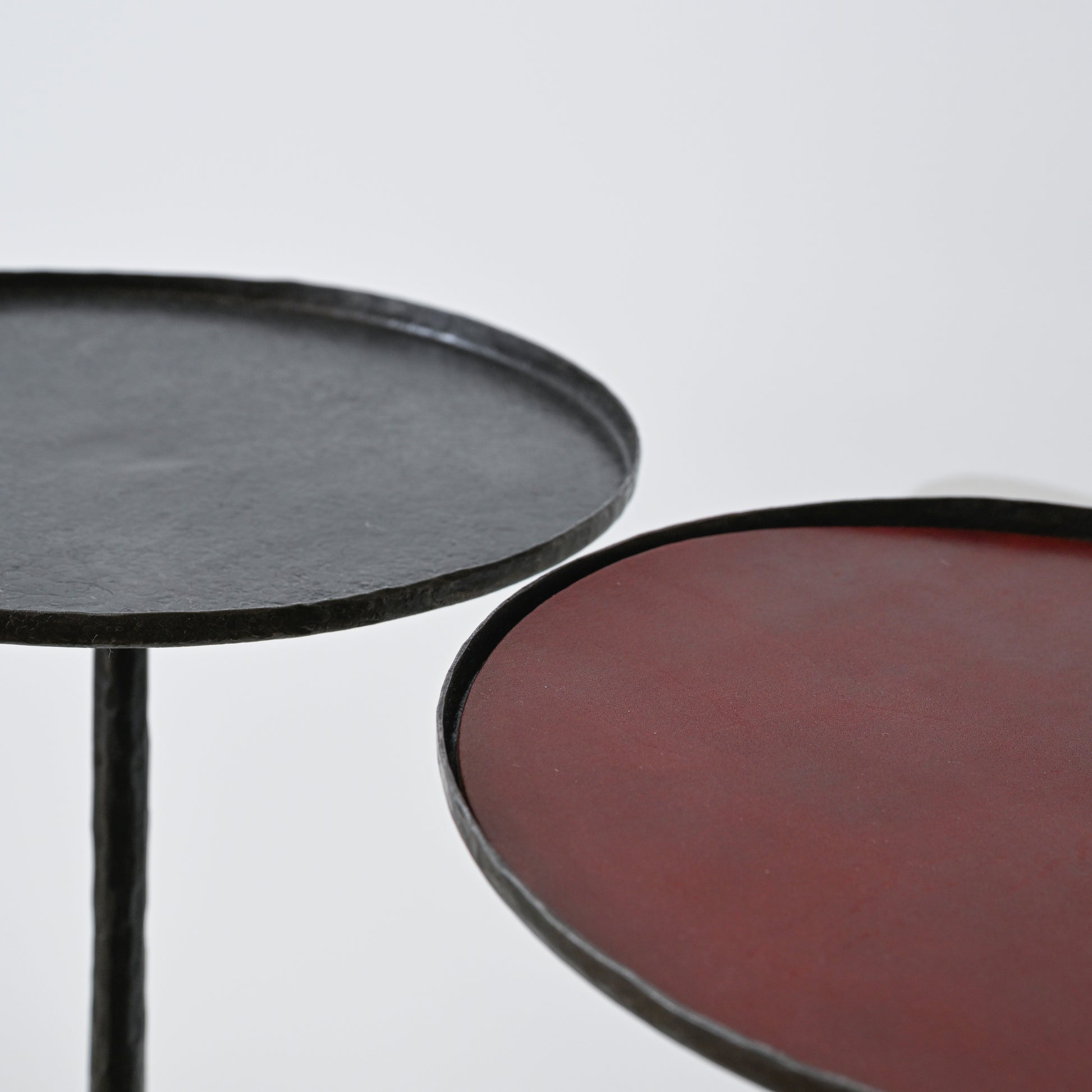 Two hand forged iron side tables with thick metal frames in matte black and rich burgundy with optional leather insert