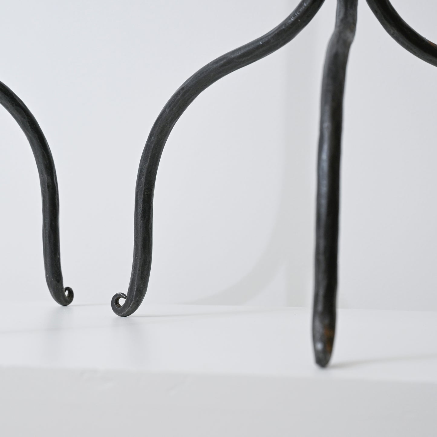 Black wrought iron legs with curved scrolled ends of hand forged iron side table visible in front view