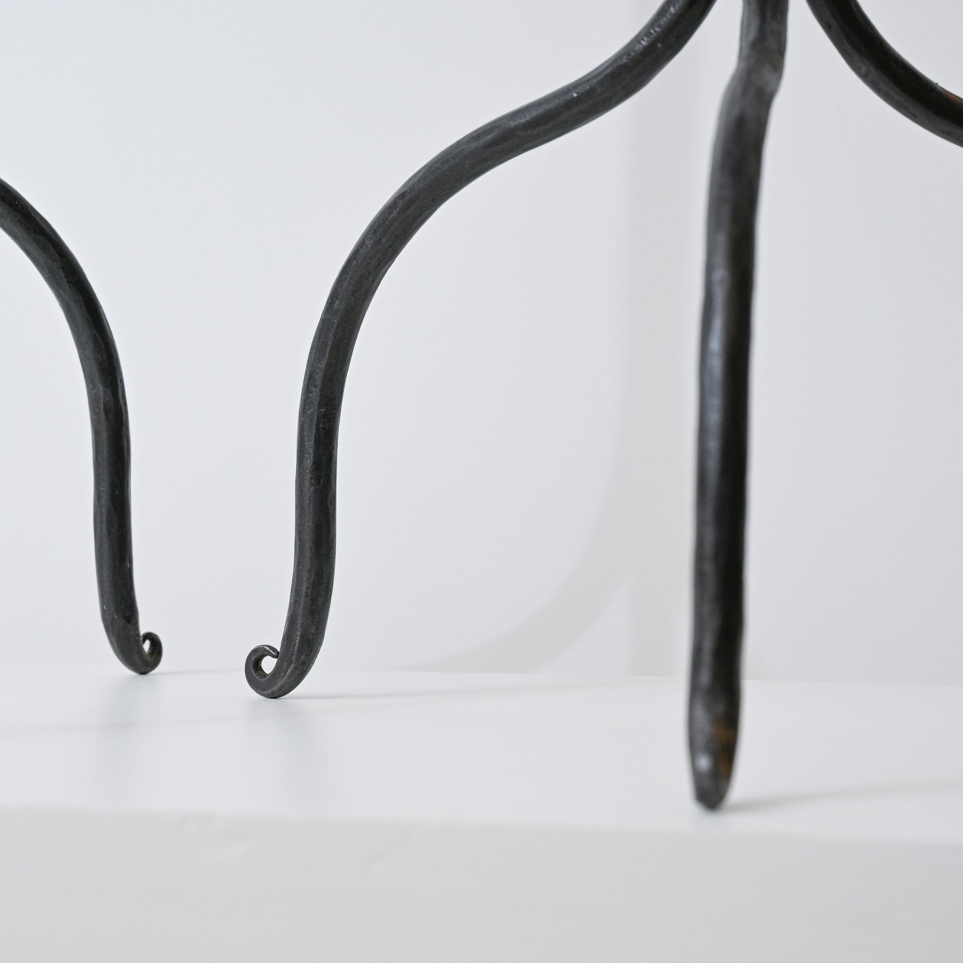 Black wrought iron legs with curved scrolled ends of hand forged iron side table visible in front view