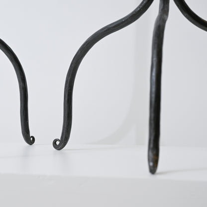 Black wrought iron legs with curved scrolled ends of hand forged iron side table visible in front view