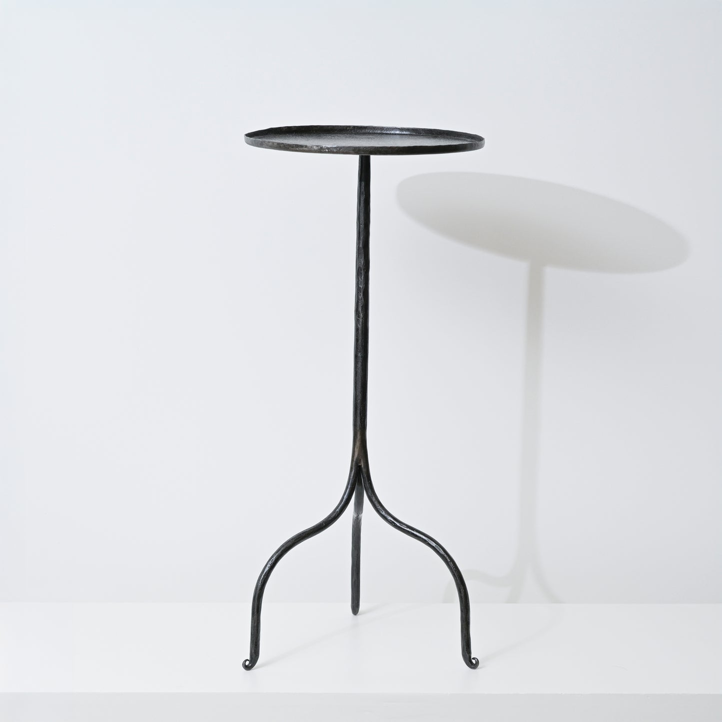 Black wrought iron tripod side table with a round slightly textured top handcrafted from hand forged iron