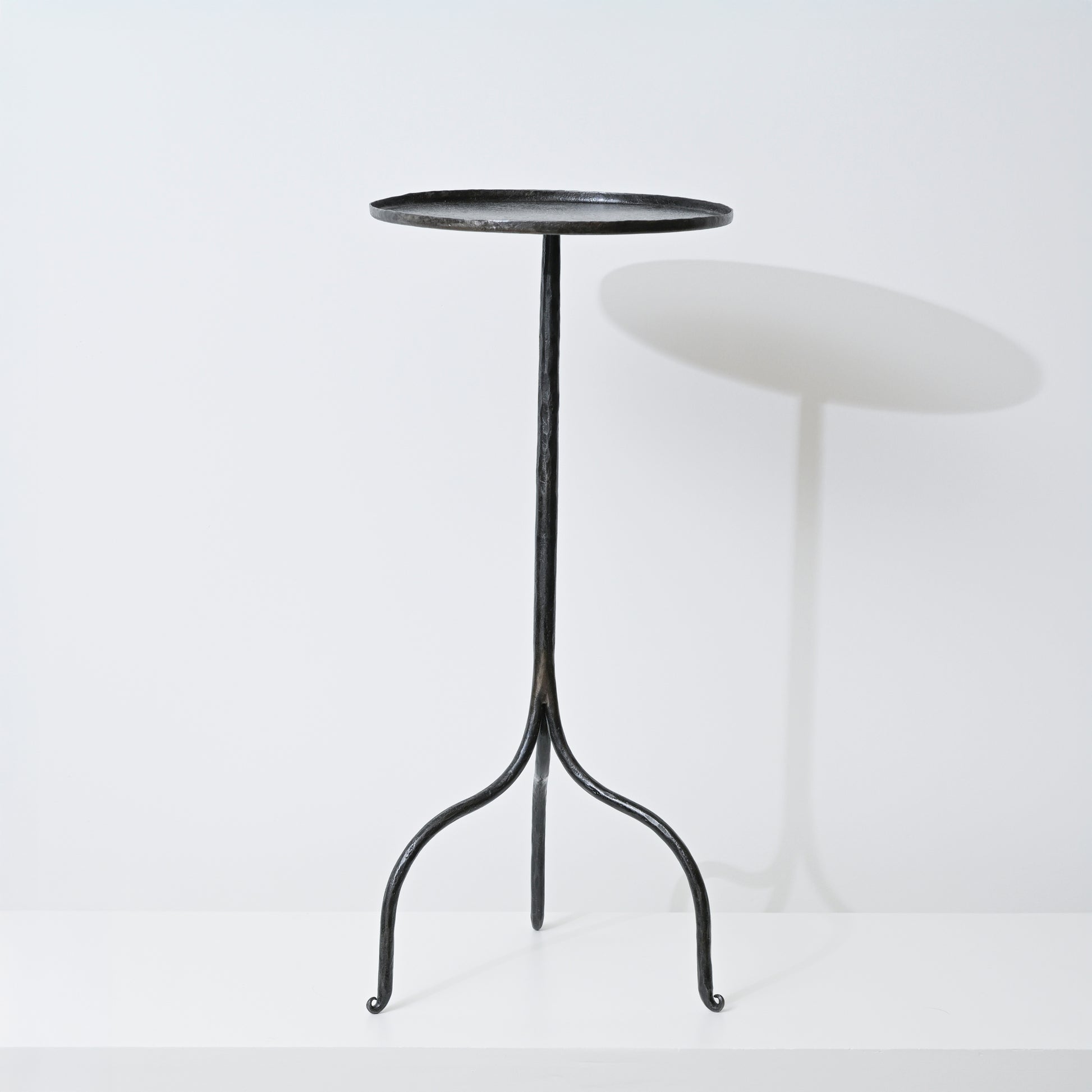 Black wrought iron tripod side table with a round slightly textured top handcrafted from hand forged iron