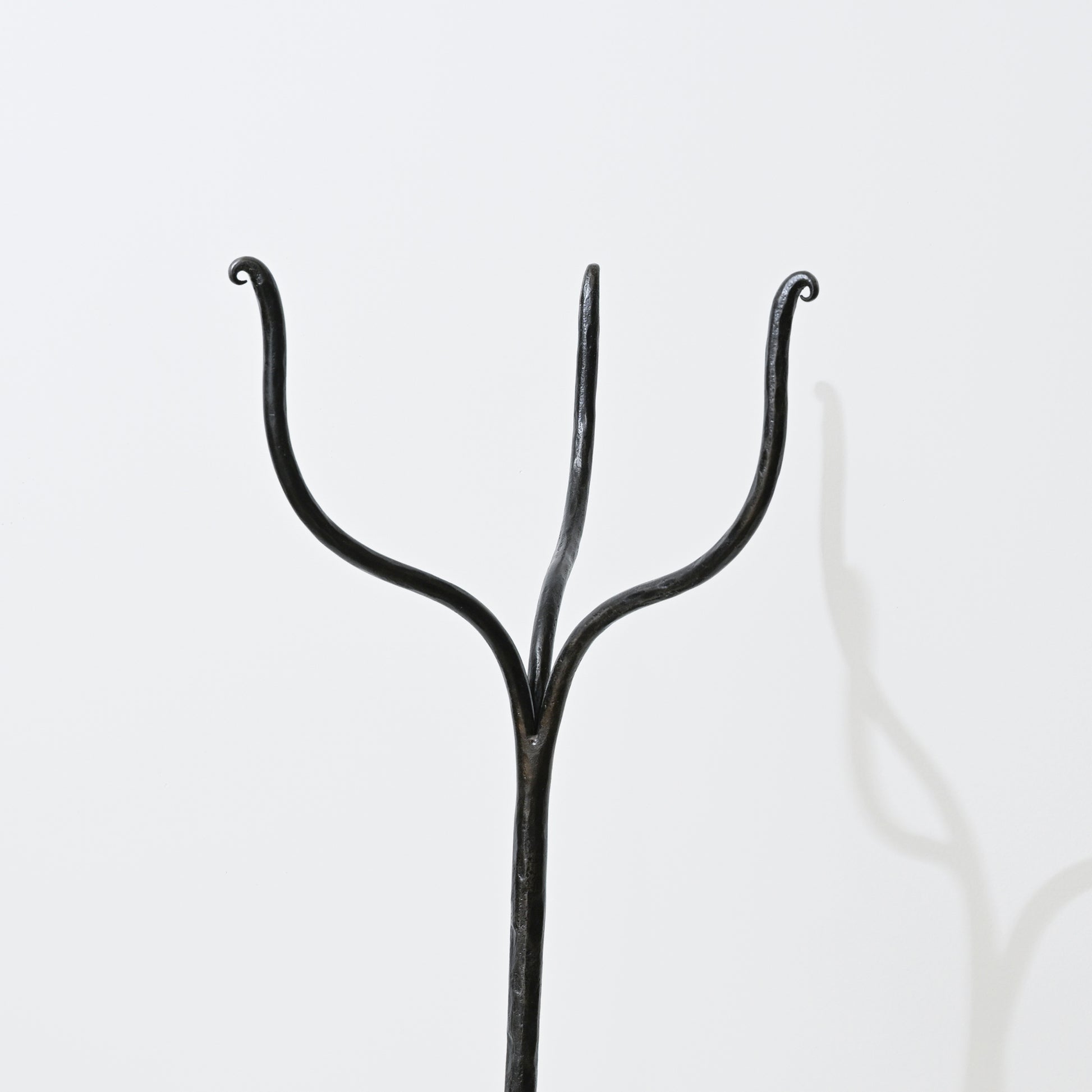 Black wrought iron coat hanger with three curved arms on hand forged iron side table
