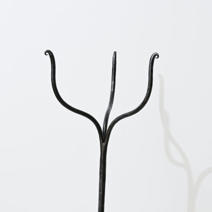 Black wrought iron coat hanger with three curved arms on hand forged iron side table