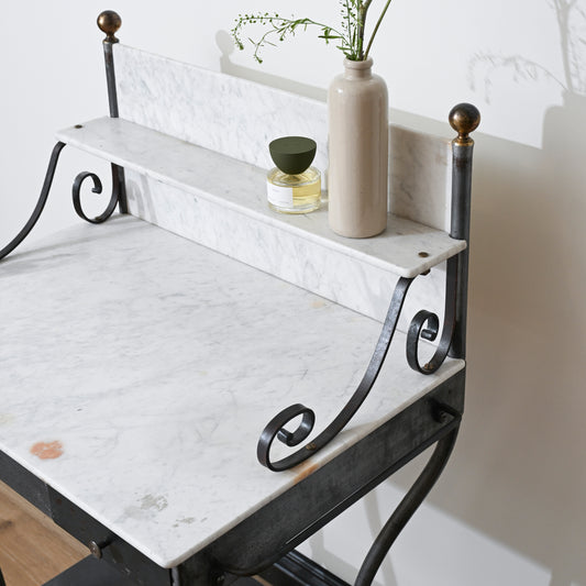 A marble-top desk with black metal legs and ornate scroll details, featuring a raised marble shelf holding a beige vase with greenery, a small glass jar, and the Antique Shanxi Ceramic Vessels (Set of 3), is set against a white wall.