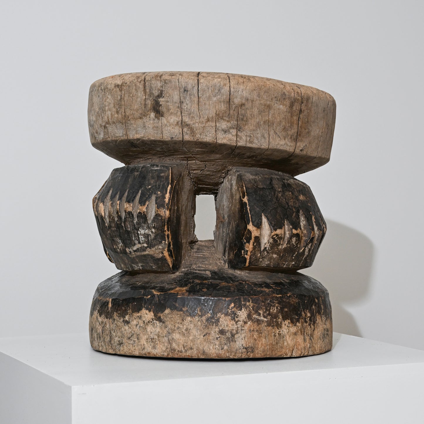 A hand carved indigenous West African dark brown wooden stool with a rounded top and faceted legs